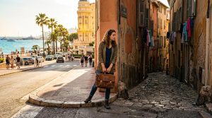 Femme avec mallette dans ruelle pavée, vue mer et palmiers
