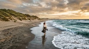 Femme marchant seule sur une plage de sable avec dunes herbeuses