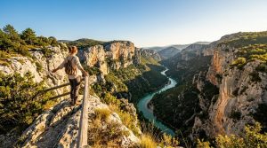 Randonneur sur une corniche surplombant un canyon avec rivière turquoise
